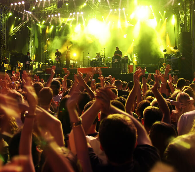 The picture shows a crowd at a concert. There is a stage in front, illuminated by green spotlights.  